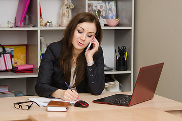 Image showing Business woman in office talking on phone and writes table