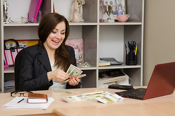 Image showing girl behind desk in office feverishly counts banknotes with a triumphant smile