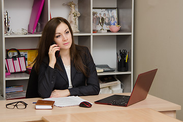 Image showing Worried office employee sitting at desk with a phone