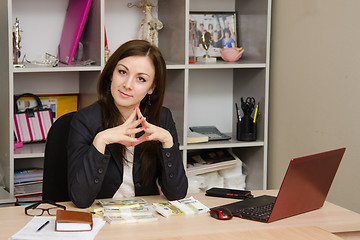 Image showing Head girl sitting at a desk with pile money her hands folded in front of him