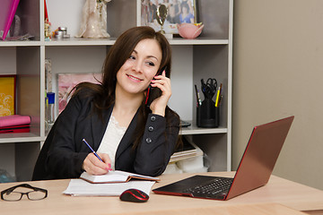 Image showing Business woman talking on phone and writes in a diary