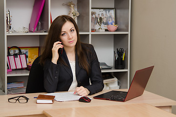 Image showing employee of the office sitting a table holding phone and looking at frame