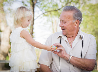 Image showing Cute Baby Girl Handing Easter Egg to Grandfather Outside