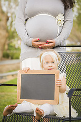 Image showing Pregnant Mom Behind Baby Girl in Chair Holding Blank Blackboard