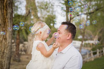 Image showing Father Holding Baby Girl Enjoying Bubbles Outside at Park