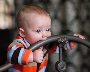 Image showing Infant Boy Blue Eyes Biting Wrought Iron Headboard