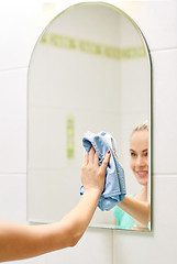 Image showing close up of happy woman cleaning mirror with rag