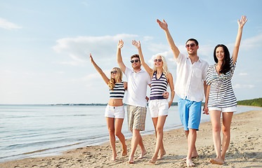 Image showing smiling friends walking on beach and waving hands