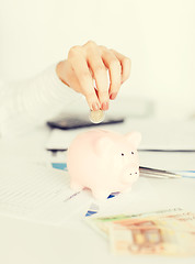 Image showing woman hand putting coin into small piggy bank