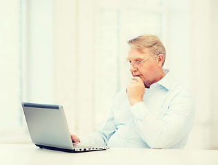 Image showing old man in eyeglasses working with laptop at home