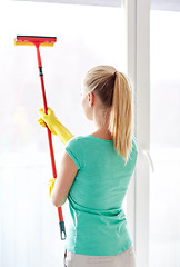 Image showing happy woman in gloves cleaning window with sponge