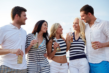 Image showing smiling friends with drinks in bottles on beach