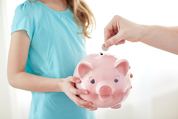 Image showing close up of girl with piggy bank putting coin