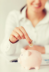 Image showing woman hand putting coin into small piggy bank