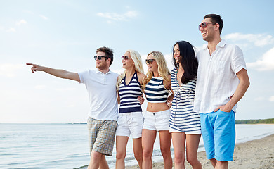 Image showing smiling friends in sunglasses walking on beach