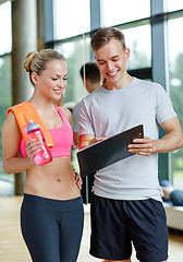 Image showing smiling young woman with personal trainer in gym