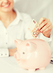 Image showing woman puts euro cash into large piggy bank