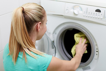 Image showing happy woman putting laundry into washer at home
