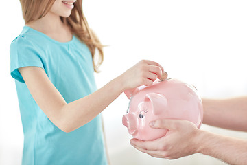 Image showing close up of girl putting coin into piggy bank