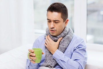 Image showing ill man with flu drinking tea and coughing at home