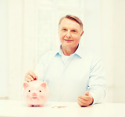 Image showing old man putting coin into big piggy bank