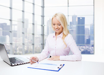 Image showing smiling businesswoman reading papers in office