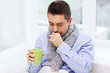 Image showing ill man with flu drinking tea and coughing at home