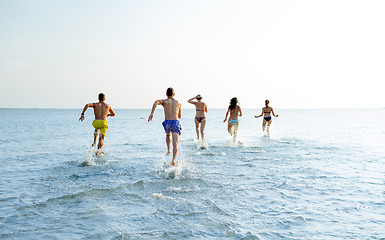 Image showing smiling friends running on beach from back