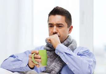 Image showing ill man with flu drinking tea and coughing at home