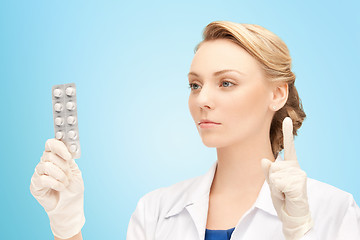 Image showing young female doctor with pills pointing finger up