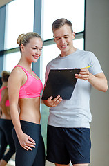 Image showing smiling young woman with personal trainer in gym