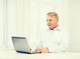 Image showing old man in eyeglasses working with laptop at home