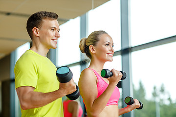 Image showing smiling man and woman with dumbbells in gym