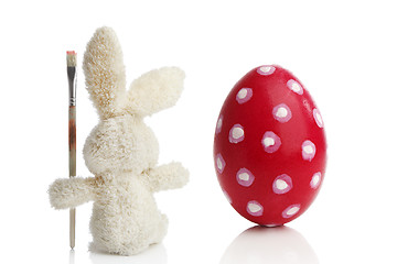 Image showing Stuffed Easter bunny paints a red Easter egg
