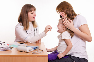 Image showing The doctor examines the throat of a child sitting on hands of mother