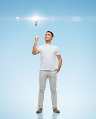 Image showing smiling man pointing finger up to lighting bulb