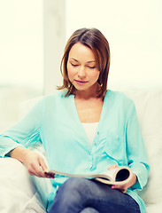 Image showing smiling woman reading magazine at home