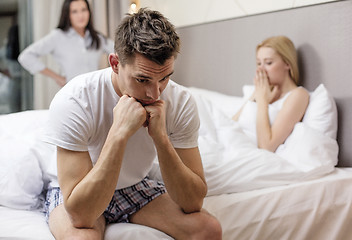 Image showing man sitting on the bed with two women on the back