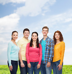 Image showing group of smiling teenagers over blue sky and grass