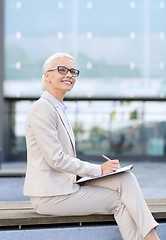 Image showing young smiling businesswoman with notepad outdoors