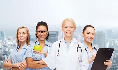 Image showing smiling female doctor and nurses with green apple