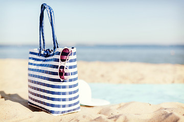 Image showing straw hat, sunglasses and bag lying in the sand