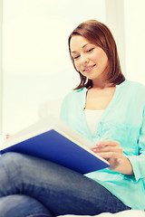 Image showing smiling woman reading book and sitting on couch