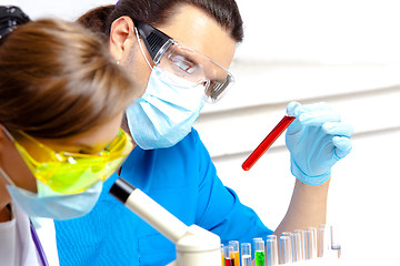 Image showing young scientist wearing a mask examines test tube with liquid