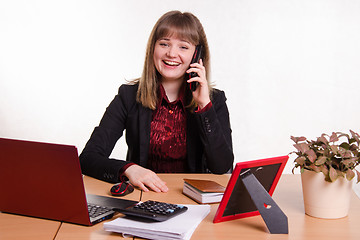 Image showing The girl behind the office desk laughing with handset