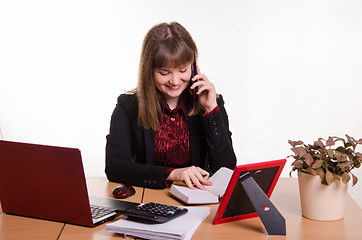 Image showing The girl behind the desk office conducts a dialogue by phone