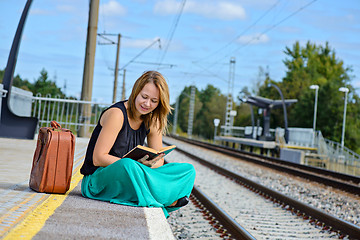 Image showing Woman sitting on the station and reading
