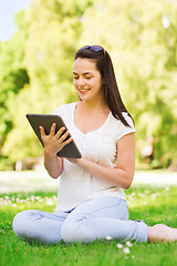 Image showing smiling young girl with tablet pc sitting on grass