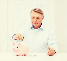Image showing old man putting coin into big piggy bank