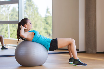 Image showing smiling woman with fit ball flexing muscles in gym